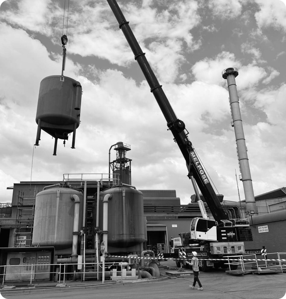 A crane lifts a large tank in front of a building.